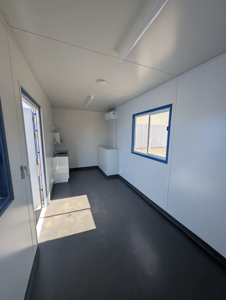 Interior of a container office looking toward the entry door, with a sink and bench