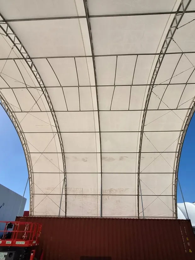 Underside of a dome tarp showing the steel truss frame and tensioning cables